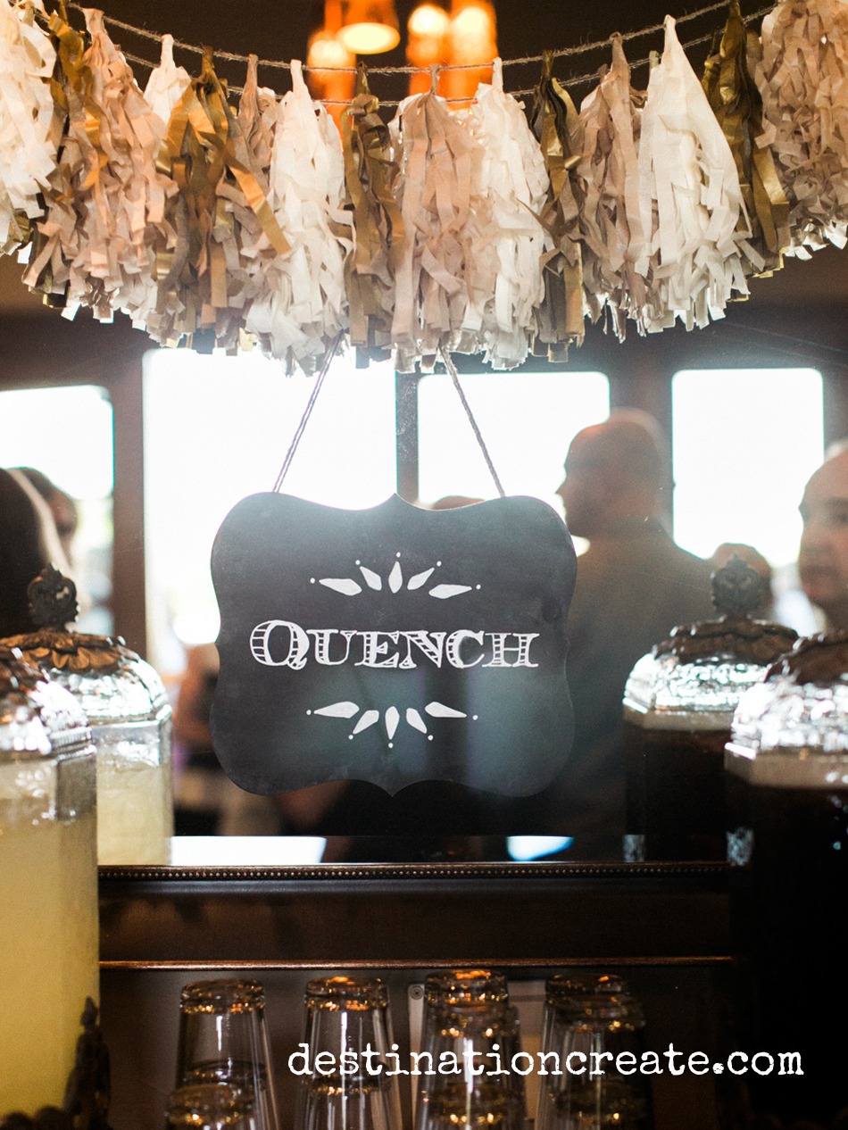 Entice wedding guests to the bar with this fun chalkboard "Quench" sign hung from a tissue paper tassel garland.